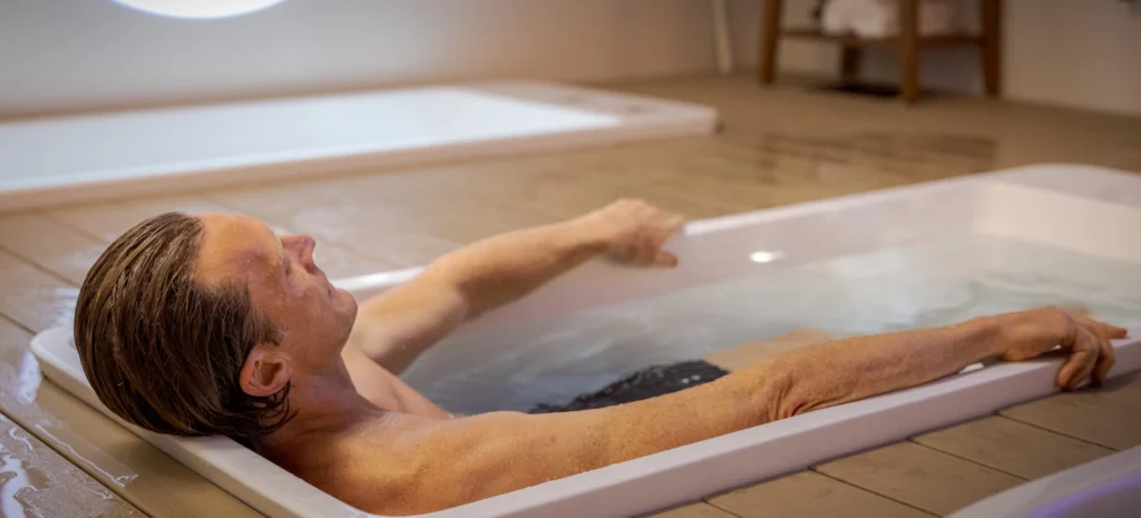 A man with his eyes closed and arms resting on the edges as he relaxes in a white cold plunge tub.
