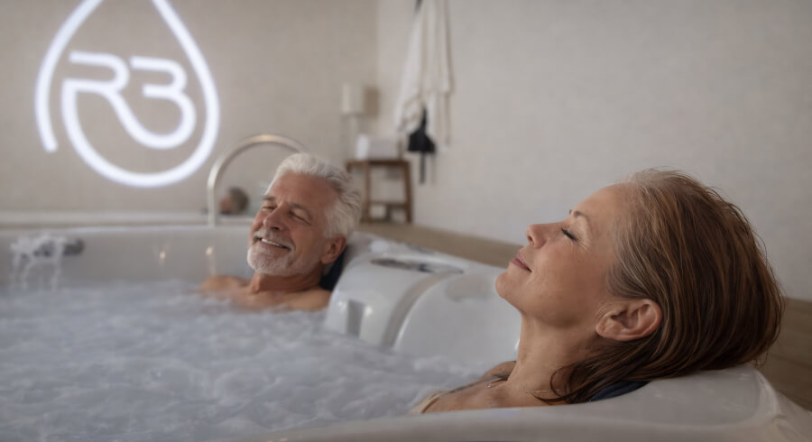 Couple relaxing in a bubbling hot tub at a wellness spa with R3 logo in the background